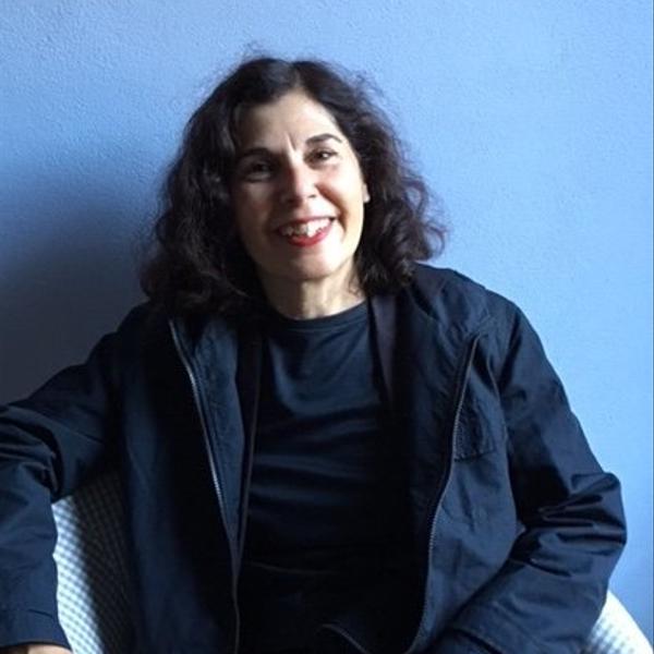 A woman with dark hair sitting in a chair with a blue background